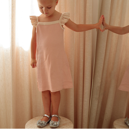 Young girl in a pink dress standing next to a mirror with a blurred reflection.