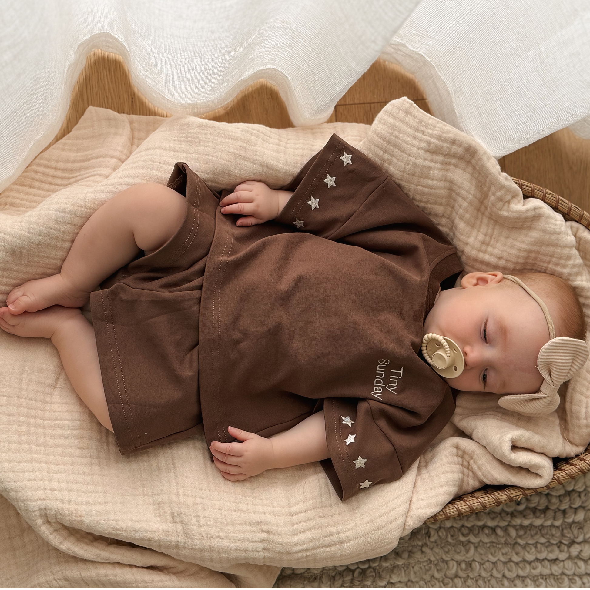 Baby in a brown outfit with star patterns lying on a beige blanket.